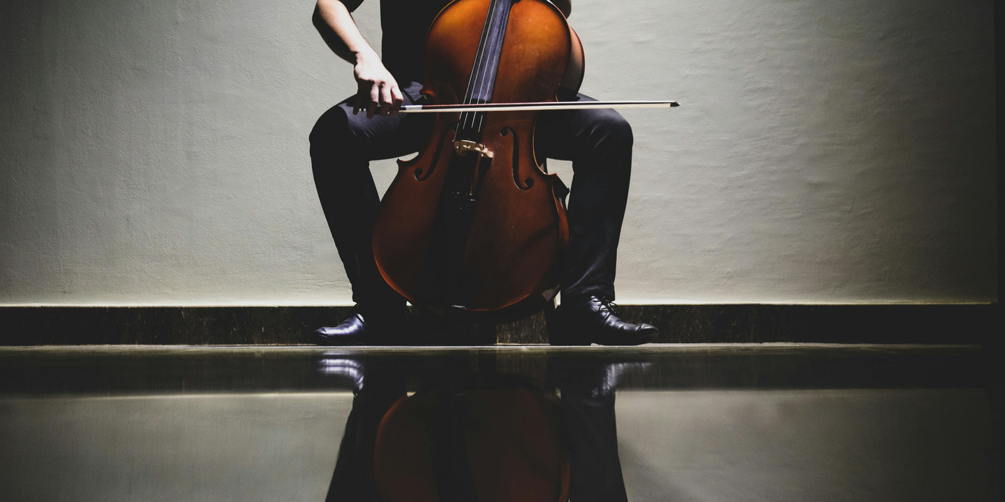 Cellist spielt im Sitzen, das Cello spiegelt sich auf glänzendem Boden.