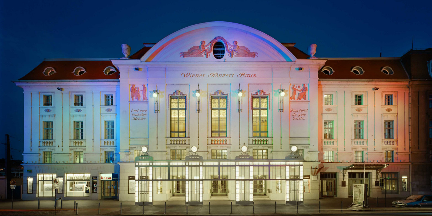 Historisches Theatergebäude bei Nacht mit bunter Beleuchtung in Blau, Weiß und Rot.