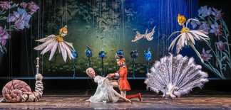 Fantasievolle Theaterszene mit Blumenfiguren, Tieren und zwei Darstellern in märchenhaftem Bühnenbild.