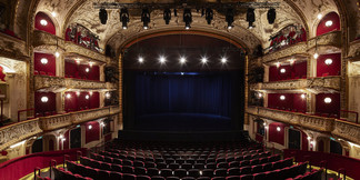 Prunkvoller Theatersaal mit rotem Interieur, goldenen Verzierungen und beleuchteter Bühne.