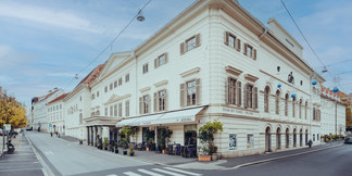 Außenansicht des Schauspielhauses Graz an einer Straßenecke mit Caféterrasse.