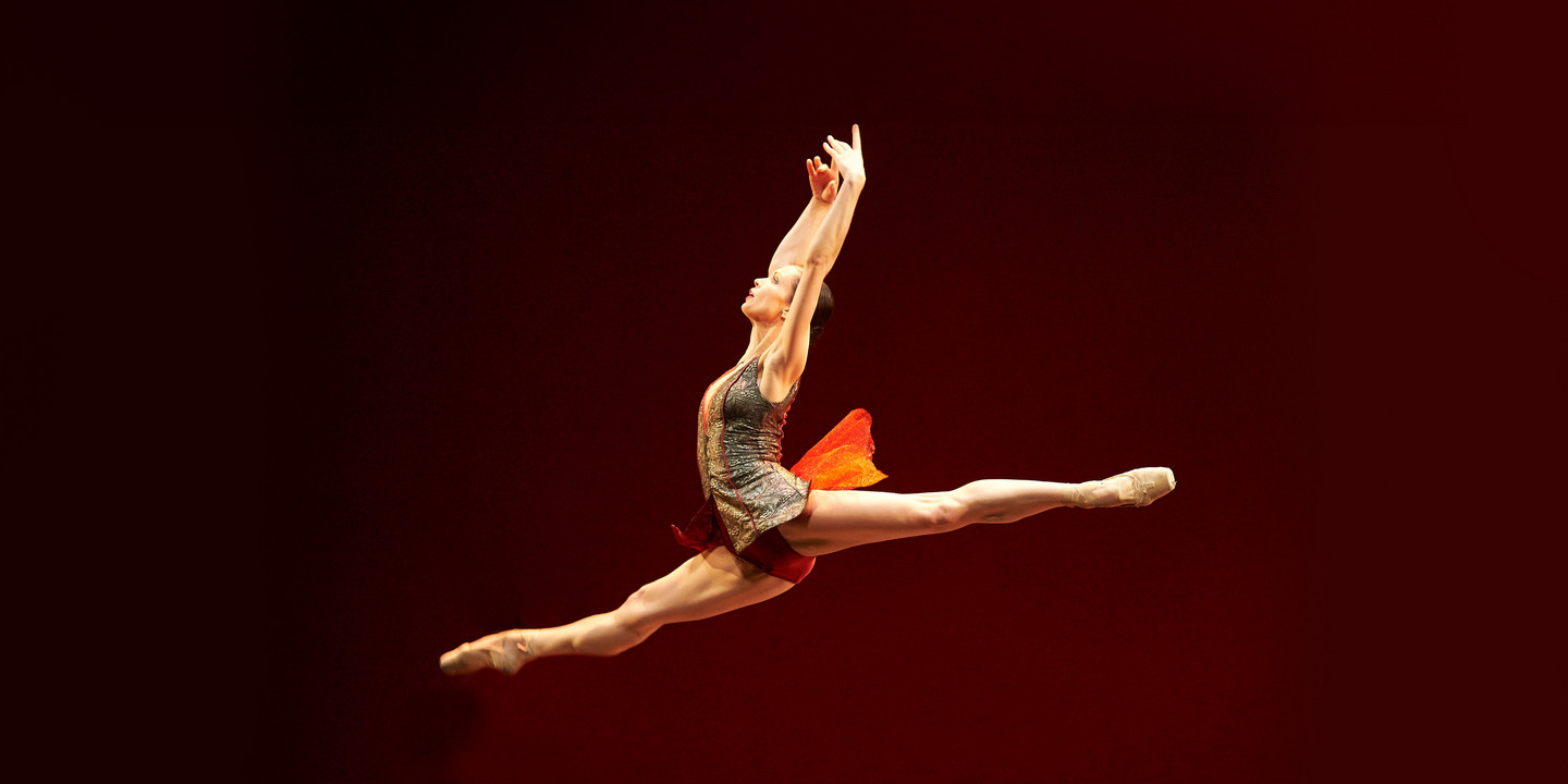 Ballerina in hohem Spagatsprung auf rot beleuchteter Bühne