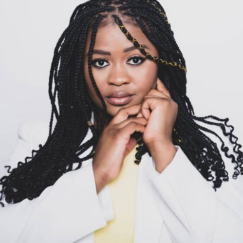 Frau mit langen Zöpfen in weißem Blazer blickt ernst in die Kamera vor hellem Hintergrund