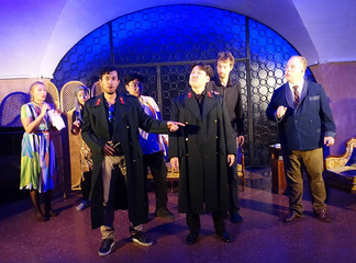 Theaterszene mit Ensemble in dunkler Kulisse und ausdrucksstarkem Lichtspiel