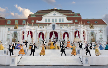 Tanzpaare in festlicher Garderobe vor barocker Schlosskulisse bei Open-Air-Veranstaltung.