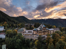 Historisches Grandhotel inmitten eines herbstlich gefärbten Waldes am Semmering, aufgenommen bei Sonnenuntergang mit dramatisch gefärbtem Himmel im Hintergrund.