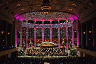 Festlich geschmückter Konzertsaal mit Orchester, Chor und Weihnachtsdekoration.