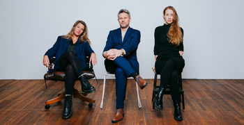 Drei Mitglieder der Leitung des Ensemble Porcia sitzen auf Stühlen vor weißer Wand
