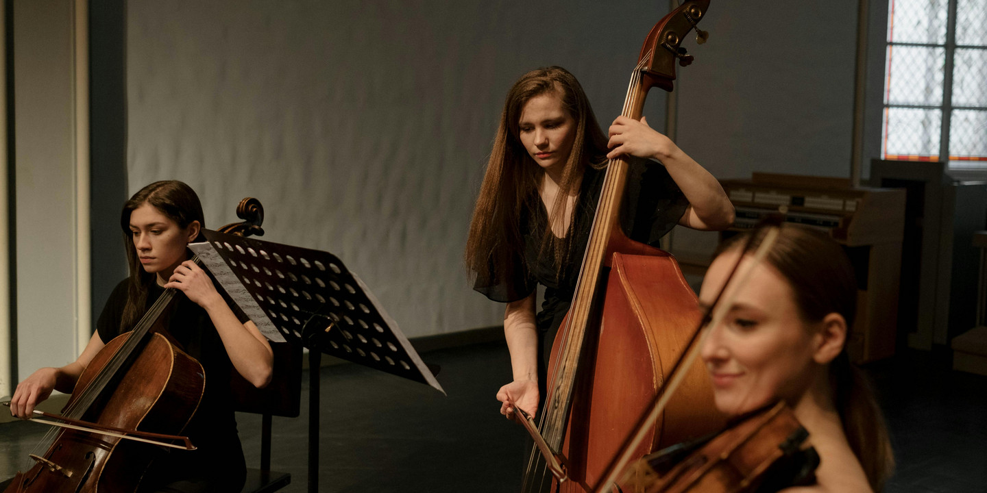 Drei Musikerinnen spielen Streichinstrumente in einem Probenraum mit Notenständer.