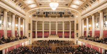 Prunkvoller Konzertsaal mit rotem Interieur, großem Kronleuchter und Publikum.