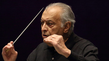 Älterer Dirigent mit erhobenem Taktstock und konzentriertem Blick vor dunklem Hintergrund.