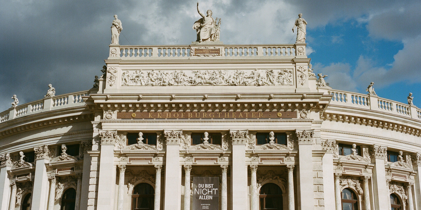 Historisches Burgtheater Wien mit Säulen, Statuen und Reliefs unter bewölktem Himmel.