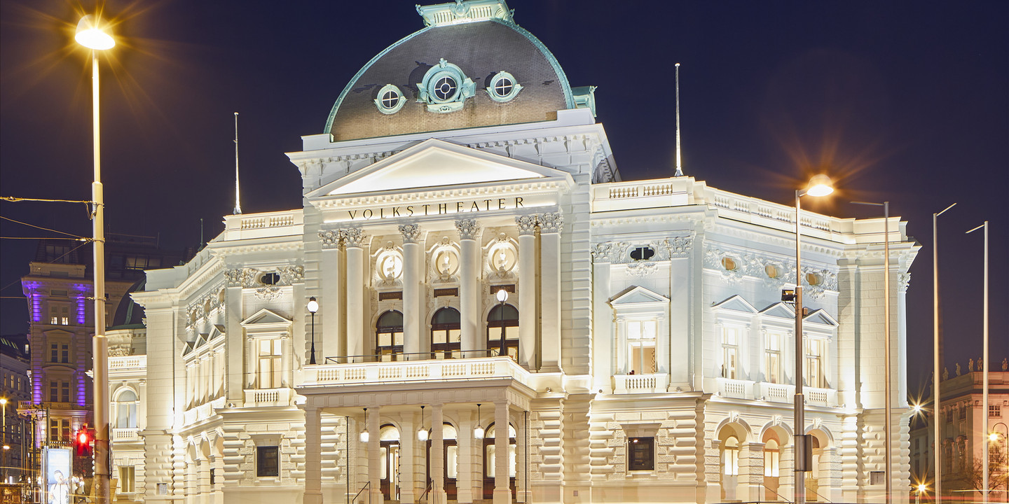 Prächtig beleuchtetes Volkstheater Wien bei Nacht.