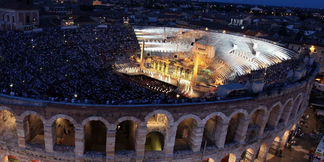Abendliche Opernaufführung in der beleuchteten Arena von Verona mit vollbesetztem Publikum.
