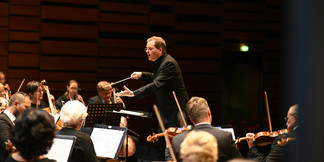 Dirigent leitet konzentriert ein Orchester auf einer modernen Konzertbühne.