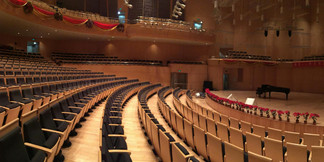 Moderner Konzertsaal mit leeren Sitzreihen, festlich geschmückter Bühne und Flügel.